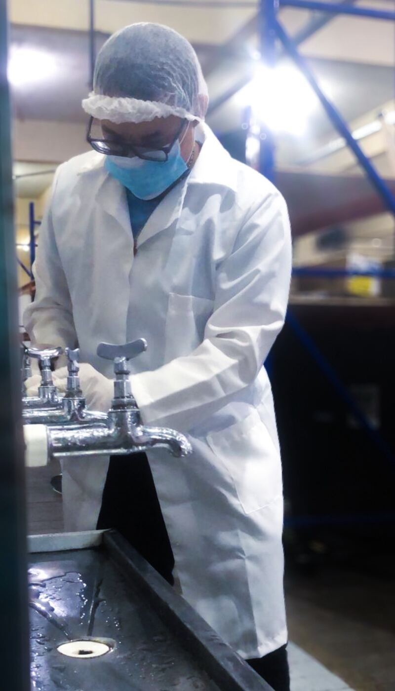 Técnico de jaleco coletando água em torneiras de área industrial